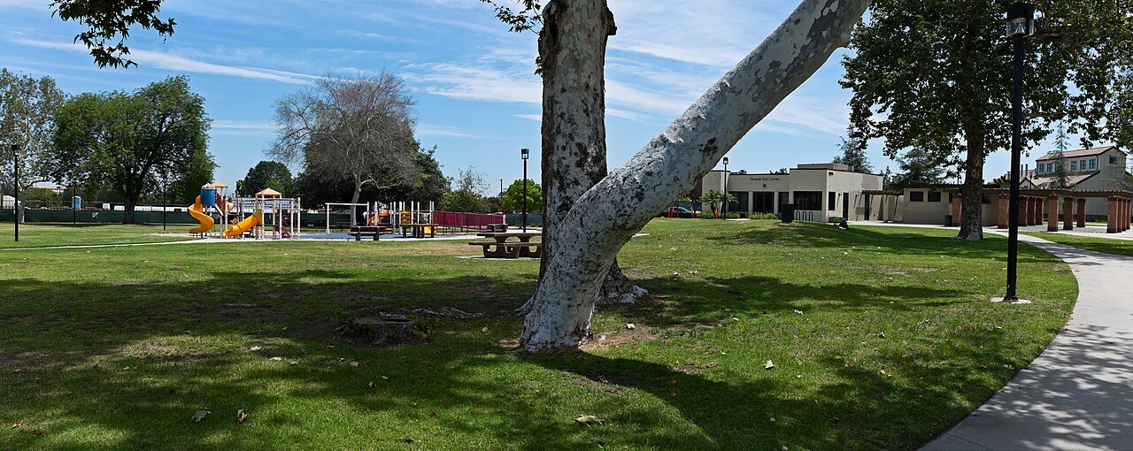 Panoramic view of a grassy park with a playground and shade trees in Norwalk, California